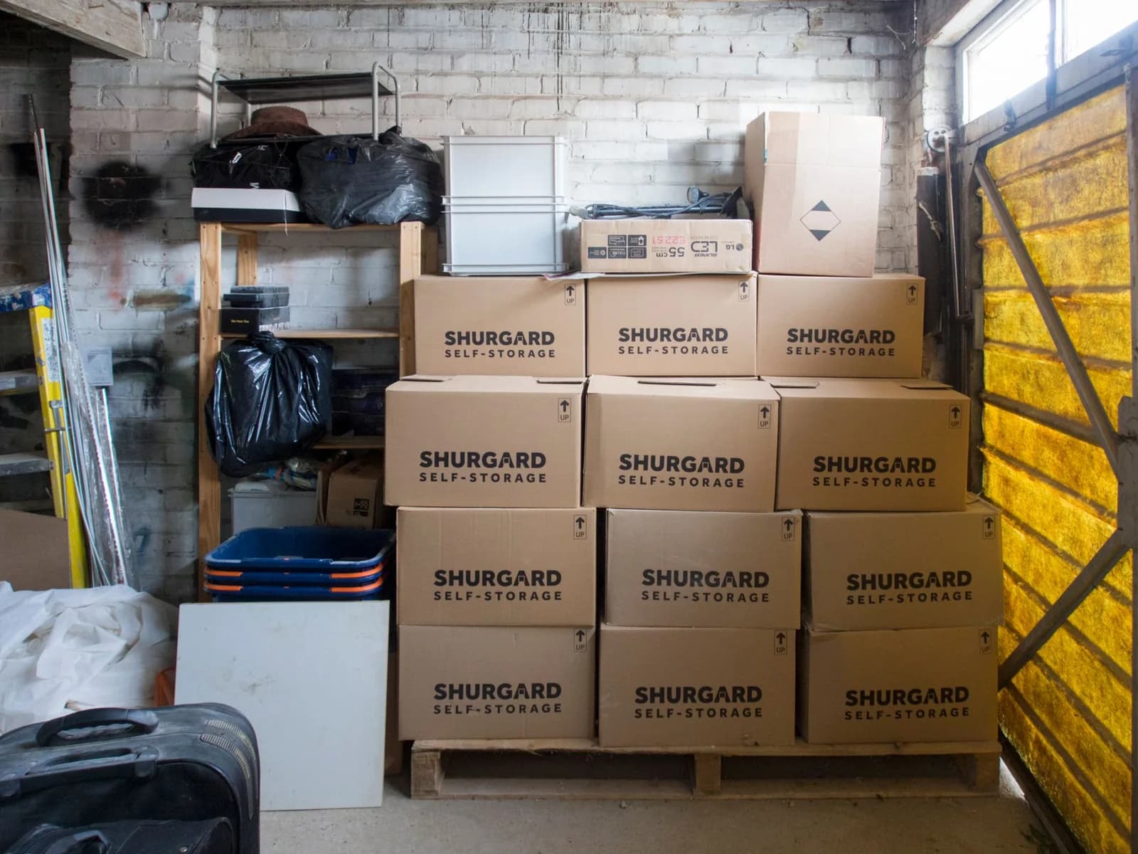 Deux box de stockage côte à côte dans un couloir de garde-meuble, porte ouverte sur des cartons